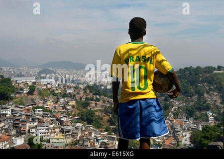 Boy, 13 years, wearing the jersey of the Brazilian national team, holding a football, overlooking slums, favela, Rio de Janeiro Stock Photo