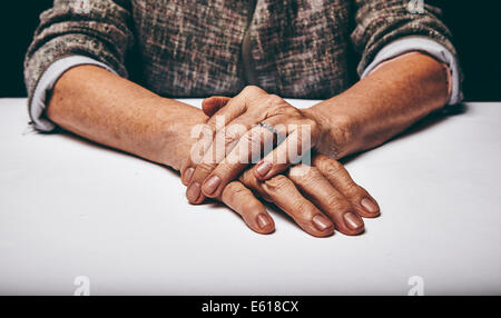 Close-up studio shot of a senior woman's hands resting on grey surface. Old lady sitting with her hands clasped on a table. Stock Photo