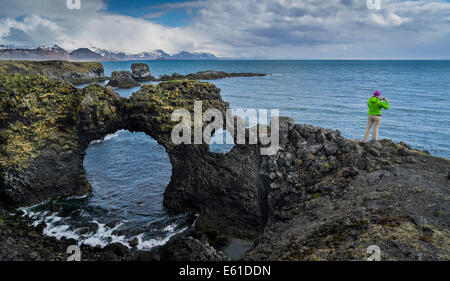 Female taking a picture of the sea while standing on the cliffs at Arnarstapi, Snaefellsnes Peninsula, Iceland Stock Photo
