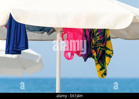 White umbrellas for protection against the sun on a sea beach and the clothes hidden under them. Stock Photo