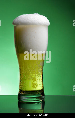 Glass of beer with froth over green background Stock Photo