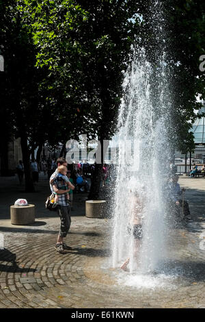 A young boy cools off from the hot weather by standing inside a water fountain on London's South Bank. Stock Photo