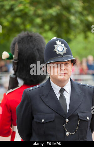 Smiling Metropolitan Police officer standing behind a foot guard on The Mall in London during Trooping the Colour Queen's Birthday Parade, London, UK Stock Photo