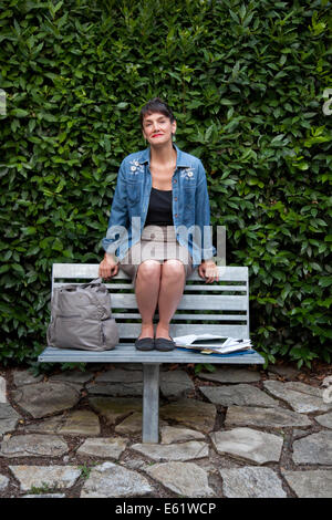 Woman sitting on a bench at the top of cliffs looking out to sea and ...