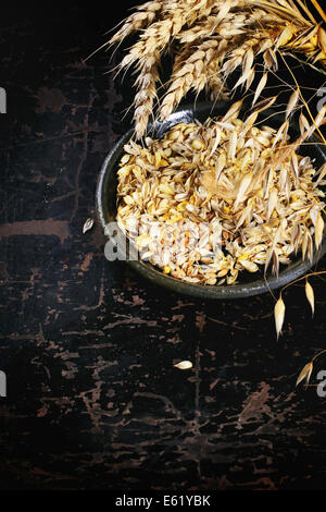 Ripe wheat and oat ears and ceramic plate of seeds over black wooden background Stock Photo