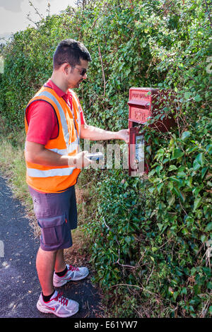 Royal Mail postman collects mail from rural pillar box Stock Photo