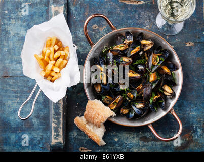 Mussels in copper cooking dish and french fries on blue background