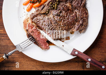 Medium rare grilled Beef steak on fork with green pepper on white plate Stock Photo