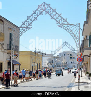 Tourists from visiting coach party walking along street in Polignano a Mare decorated arches erected for local festival Province of Bari Apulia Puglia Stock Photo