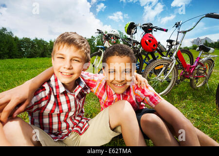 Two best friends sit on grass and hug with arms Stock Photo