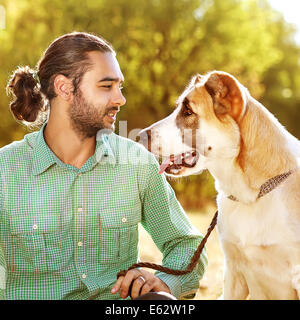 Man and central Asian shepherd walk in the park. He keeps the dog on the leash. Stock Photo