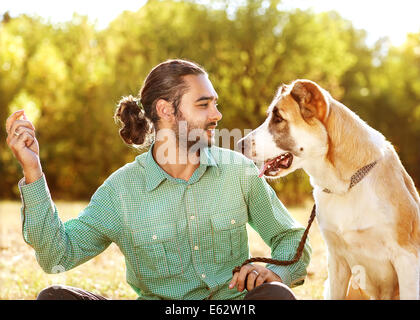 Man and central Asian shepherd walk in the park. He keeps the dog on the leash. Stock Photo
