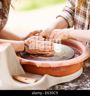 Female Potter creating a bowl on a Potters wheel, the master potter helping her Stock Photo