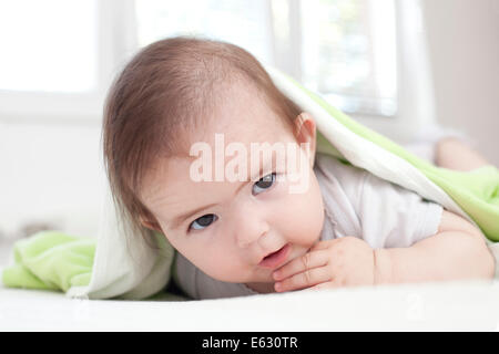 Baby girl is hiding under the white and green blanket Stock Photo