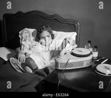1950s GIRL SICK IN BED PLAYING RECORDS HOLDING BABY DOLL Stock Photo