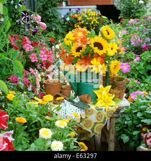 1990s FLOWERS IN WATERING CAN FLOWER POTS AND TROWEL ON TABLE IN GARDEN Stock Photo