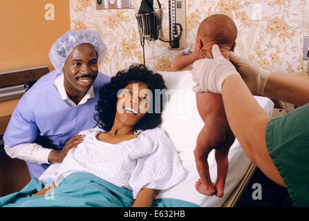 1980s AFRICAN AMERICAN MOM AND DAD VIEW NEWBORN INFANT IN HOSPITAL BERTHING ROOM Stock Photo