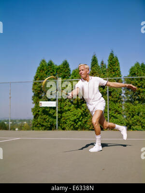 1960s BLONDE MAN WEARING TENNIS WHITES FOLLOWING THROUGH AFTER HITTING BALL Stock Photo