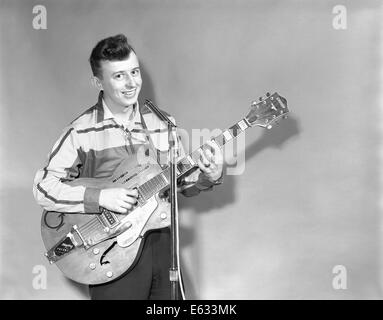 1950s TEENAGE BOY SINGING PLAYING GUITAR INTO MICROPHONE Stock Photo