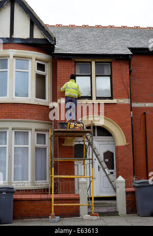 Man on scaffold tower repointing the brickwork on the front of a terraced house Stock Photo