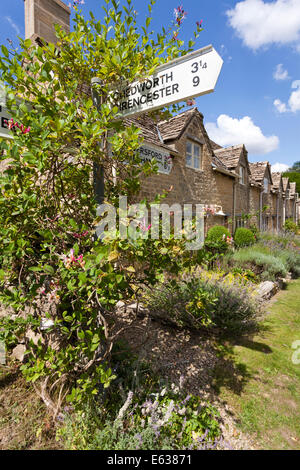 Honeysuckle growing up the road sign in front of stone cottages in the Cotswold village of Withington, Gloucestershire UK Stock Photo