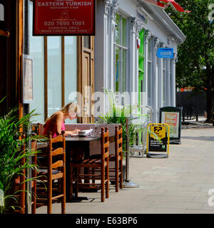 blond woman sitting writing letter & having coffee at Eastern Turkish Restaurant in London Stock Photo