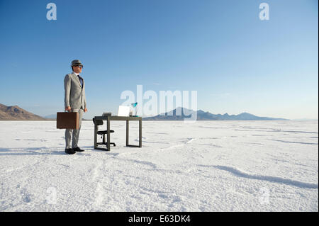 Businessman standing next to mobile office desk outdoors on dramatic white desert landscape Stock Photo