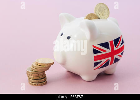 British Union Jack on Piggy bank looking at a pile of sterling pounds  pound coins illustrating savings and financial growth concept. UK Britain Stock Photo