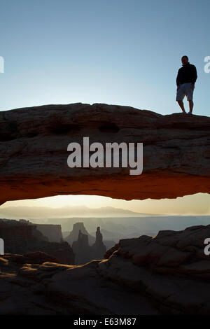 Person on Mesa Arch and sunrise over La Sal Mountains, Canyonlands National Park, Utah, USA