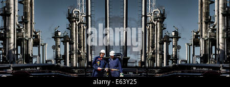 two oil-workers standing in front of large refinery industry Stock Photo