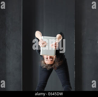 Young woman bending over backwards and reading on tablet computer upside down. Stock Photo