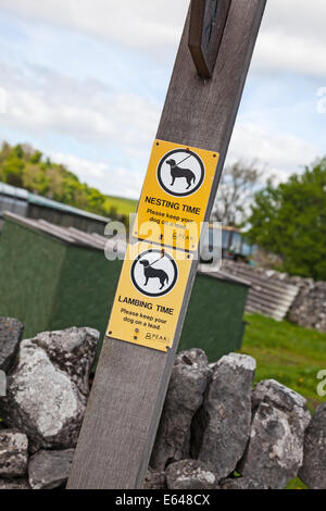 A sign on a wooden footpath signpost saying keep dogs on a lead during nesting  time and lambing time Stock Photo