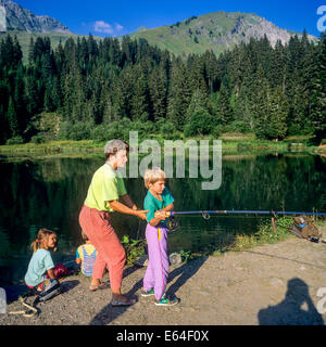 Woman teach angling to boy at Les Mines d'Or lake Morzine resort Savoy French Alps France Stock Photo