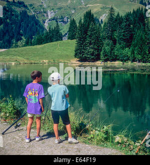 Two boys angling at Les Mines d'Or lake Morzine resort Savoy French Alps France Europe Stock Photo