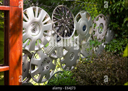 Found car  wheel hubs used for decorating a wire fence in a small garden Stock Photo