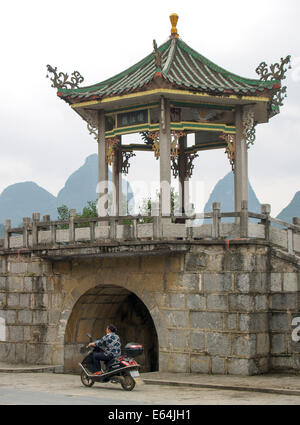 Scooter rides past roadside temple in Guilin China against dramatic limestone karst landscape Stock Photo