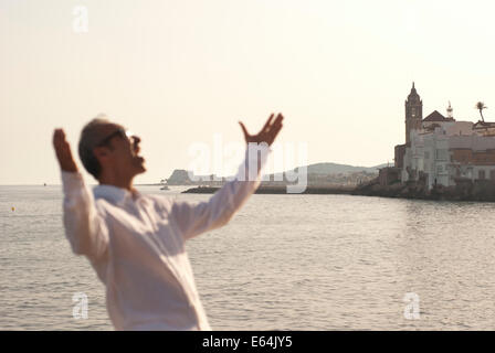 Mature Man standing with arms outstretched smiling and screaming with the sea in background Stock Photo