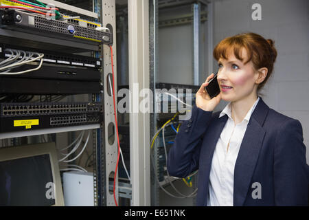 Pretty computer technician talking on phone beside open server Stock Photo
