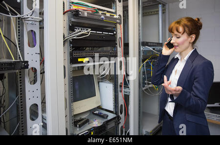 Pretty computer technician talking on phone beside open server Stock Photo