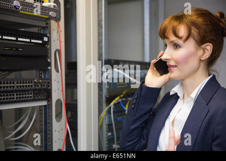 Pretty computer technician talking on phone beside open server Stock Photo