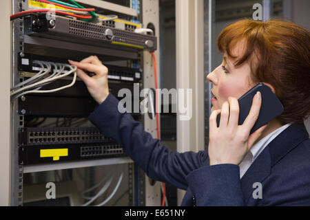 Pretty computer technician talking on phone while fixing server Stock Photo