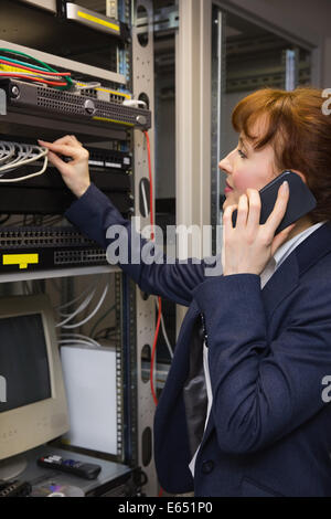 Pretty computer technician talking on phone while fixing server Stock Photo