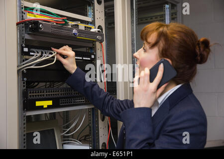 Pretty technician talking on phone while fixing server Stock Photo