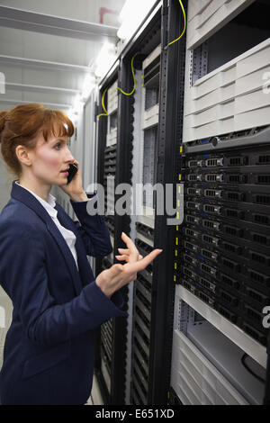 Pretty technician talking on phone while looking at server Stock Photo