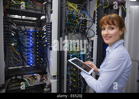 Smiling technician using tablet pc while analysing server Stock Photo