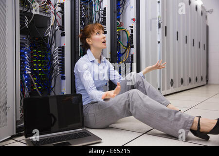 Stressed technician sitting on floor beside open server Stock Photo