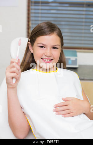 Little girl holding toothbrush in dentists chair Stock Photo