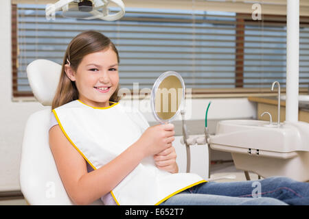 Little girl holding mirror in dentists chair Stock Photo