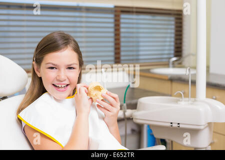 Little girl sitting in dentists chair holding model teeth Stock Photo