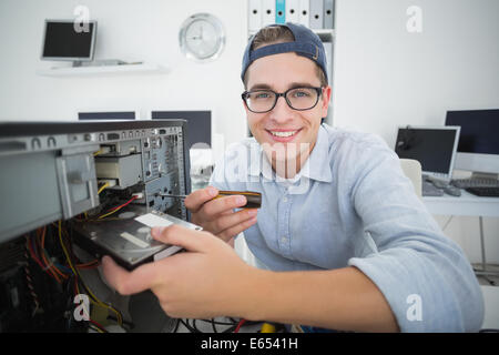 Smiling computer engineer working on broken console with screwdriver Stock Photo